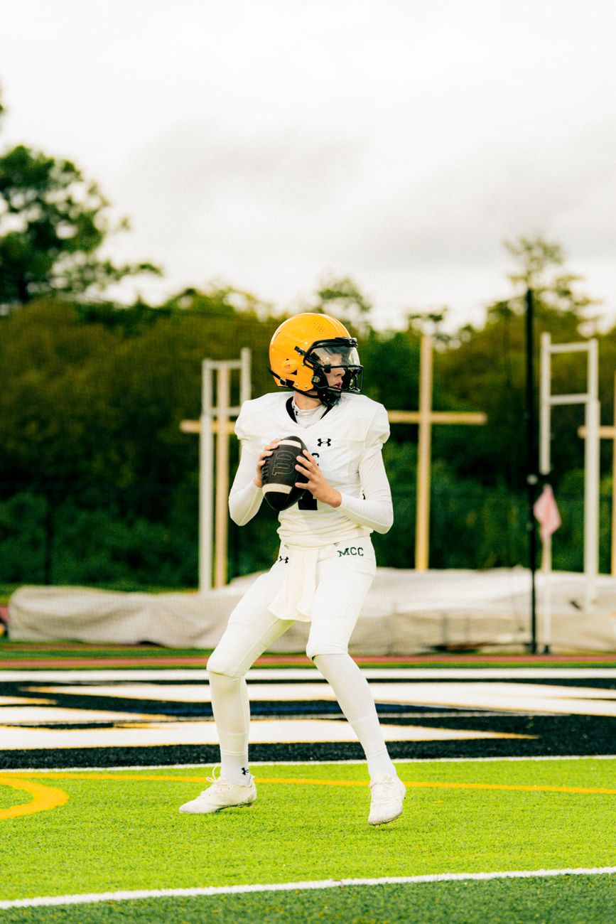 A young football player in full gear preparing to make a pass on an outdoor field.