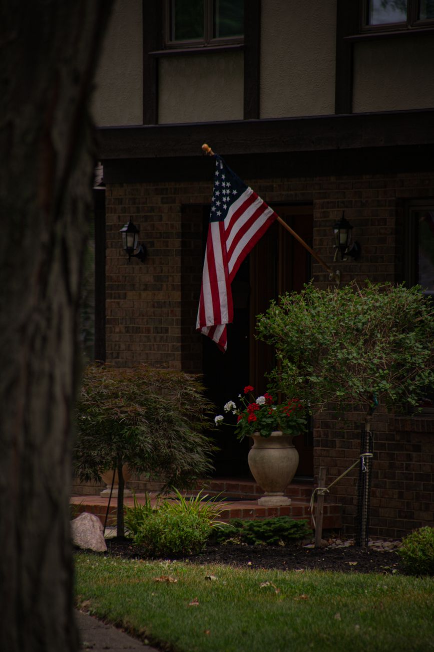 Charming suburban house entrance with American flag and lush garden.