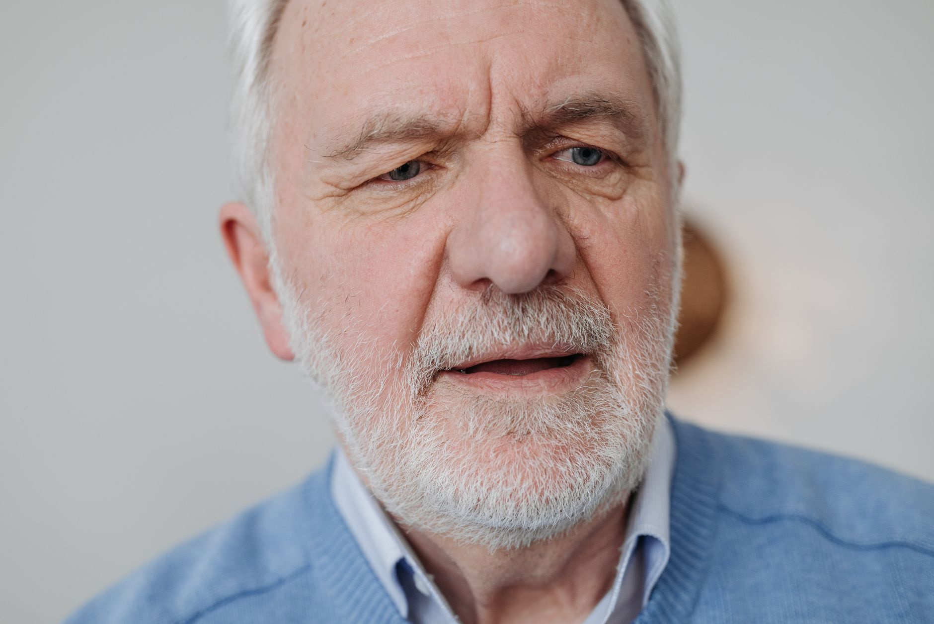 Close up portrait of an elderly man with white hair and beard, wearing a blue sweater.