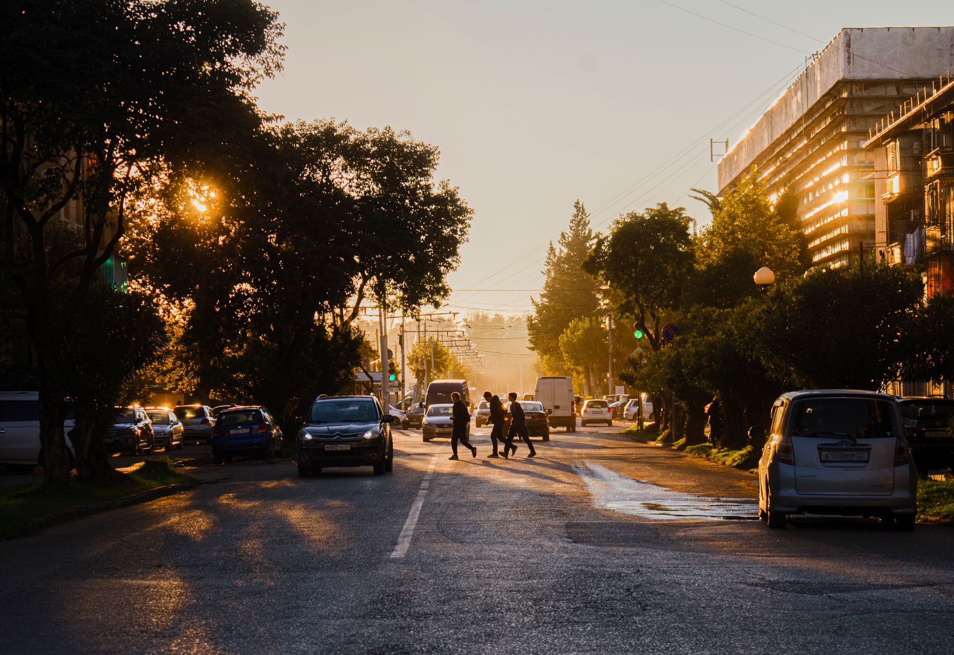 City street scene at sunset with silhouettes of pedestrians and cars in warm light.