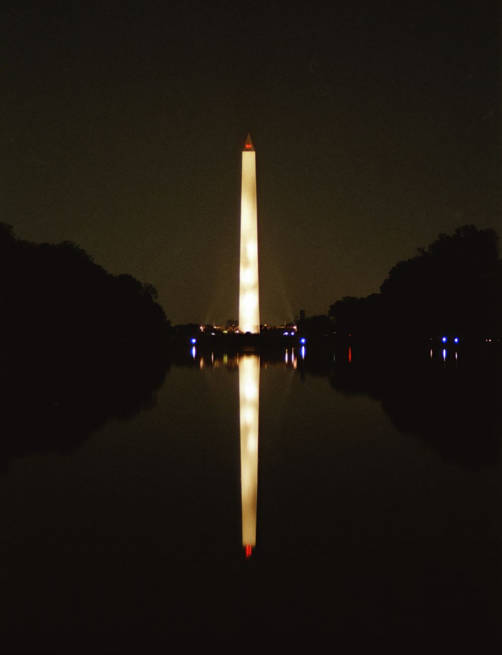 The Washington Monument illuminated at night, reflected in the water, creating a serene and iconic view of Washington, DC.