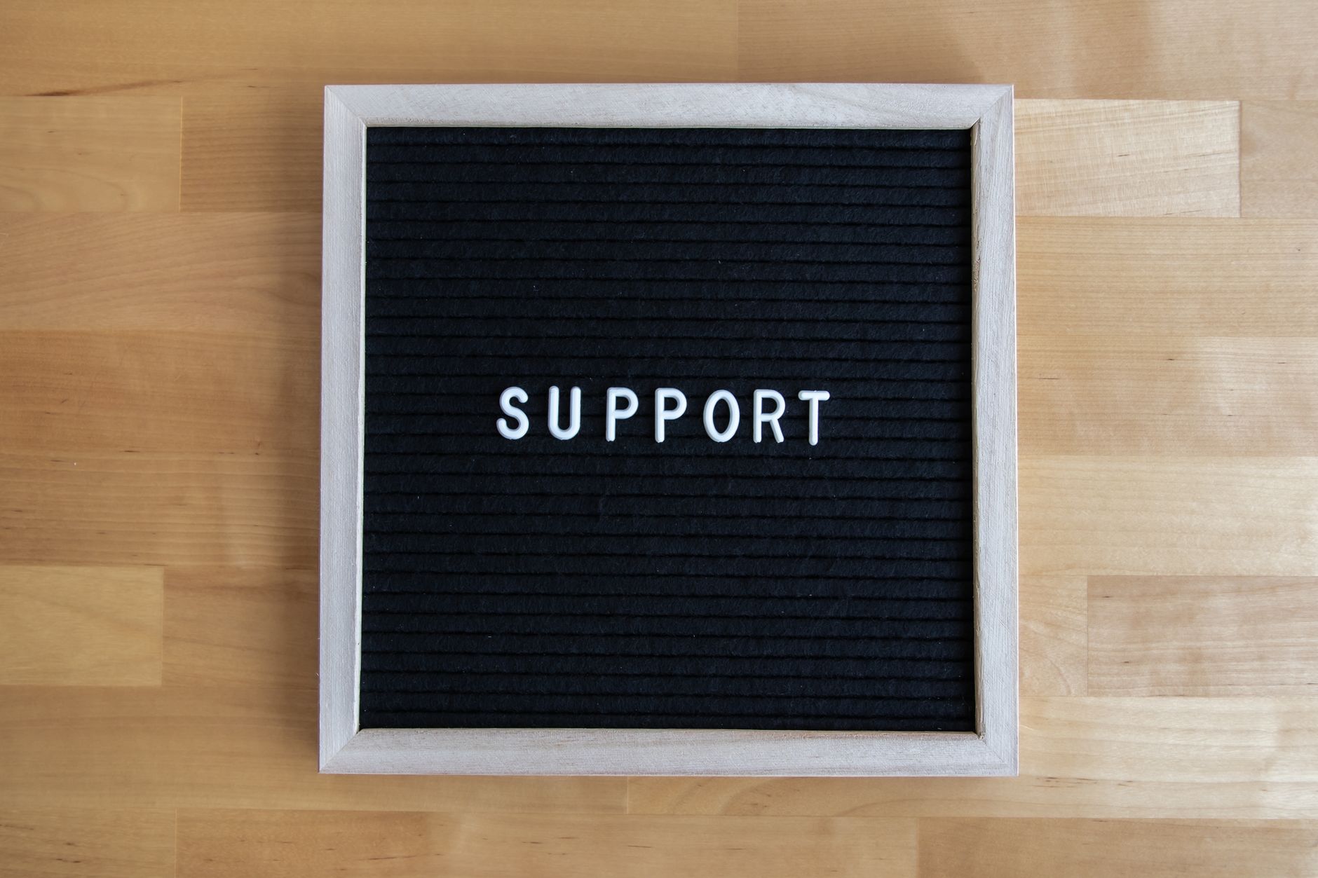Black letter board displaying the word SUPPORT on a wooden table, offering ample copyspace.