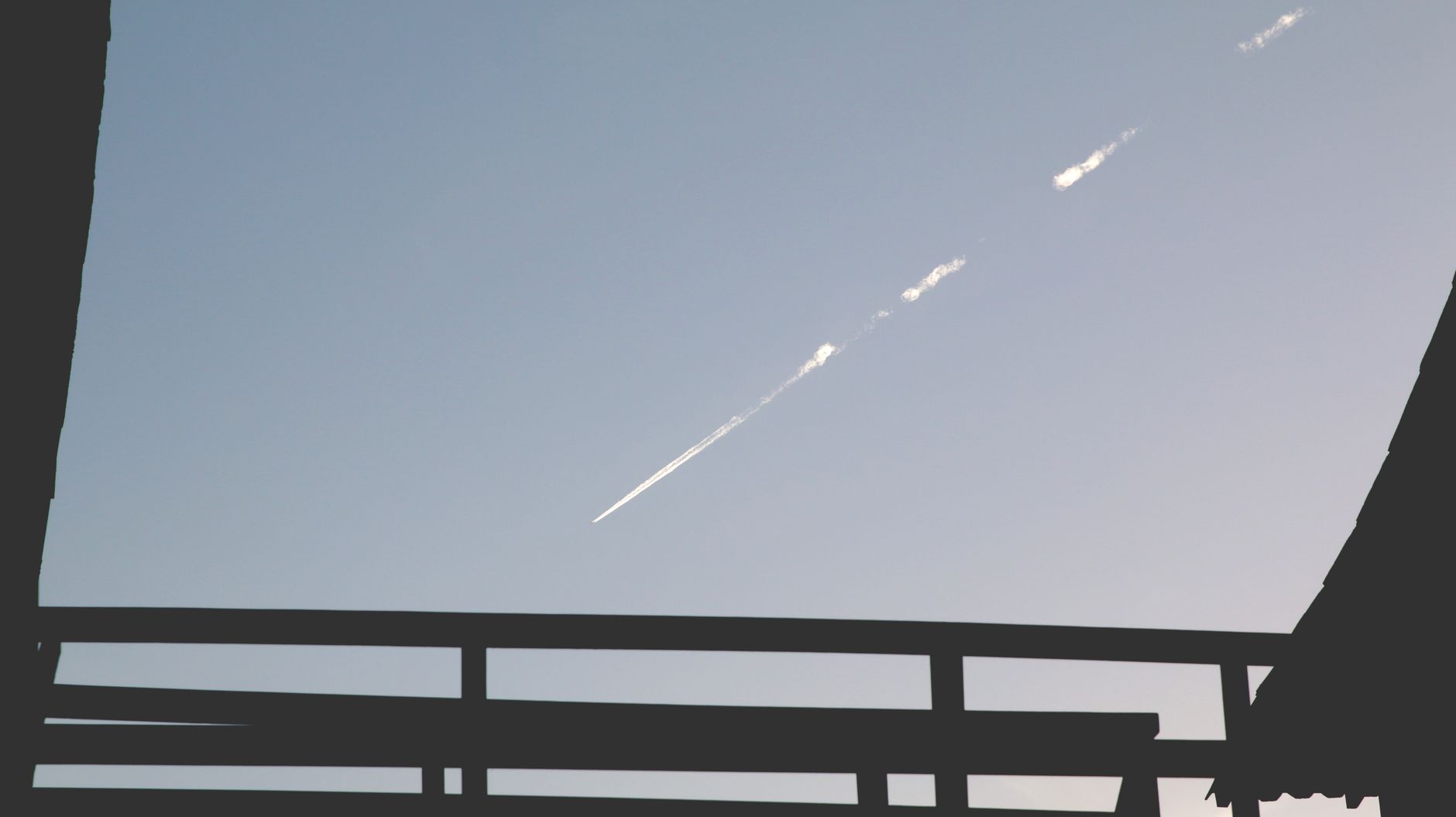 Silhouette of a structure with a jet contrail in the clear blue sky contrasted against it.