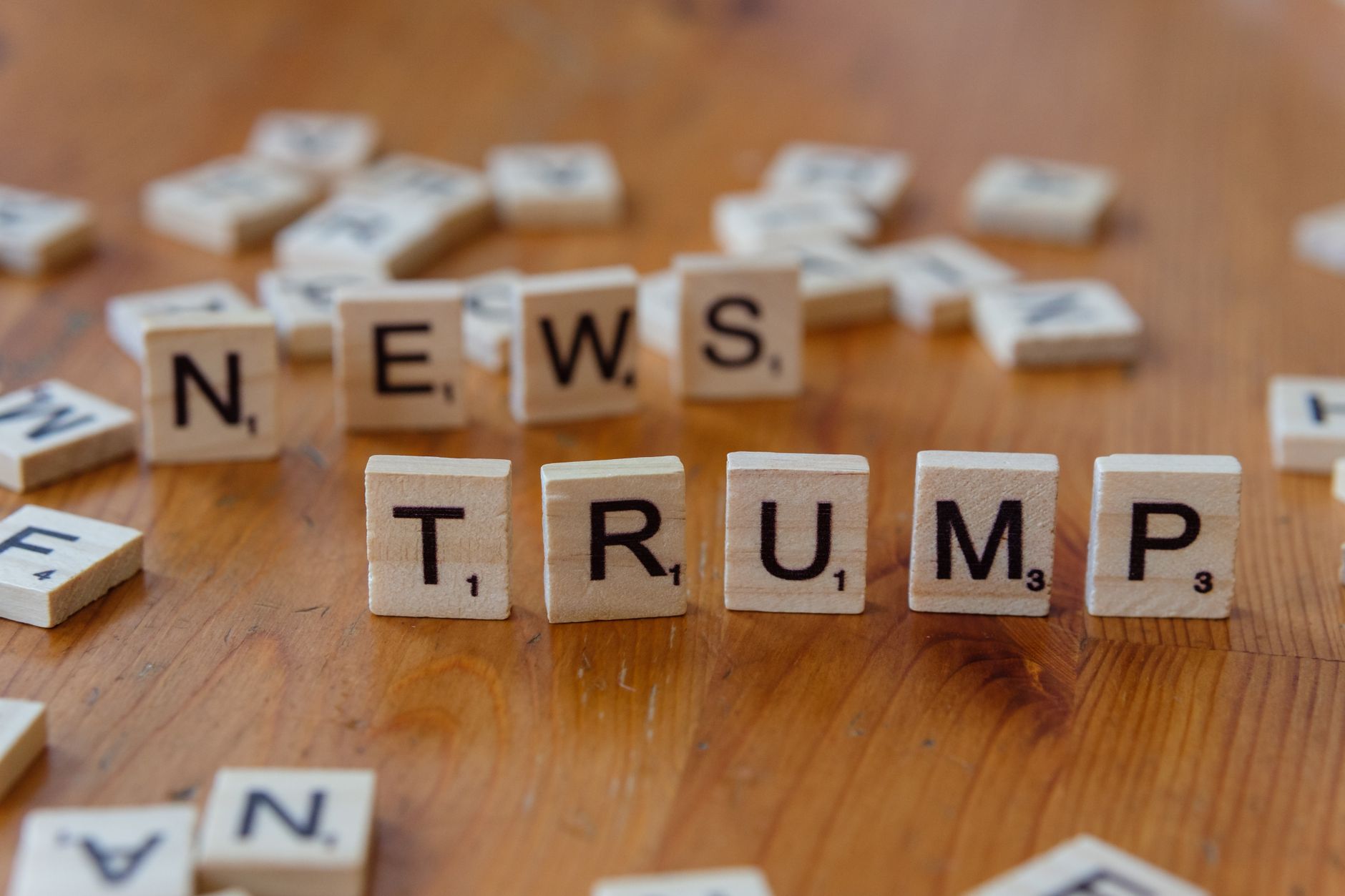 Wooden letter tiles spell &amp;#39;NEWS&amp;#39; and &amp;#39;TRUMP&amp;#39; on a wooden table, relating to political discourse.