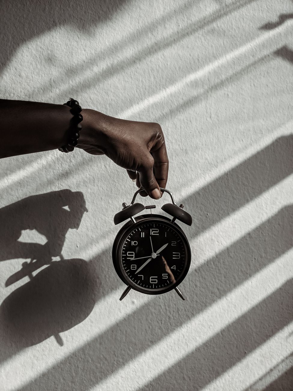 Close up of a hand holding a vintage alarm clock casting shadows in daylight.