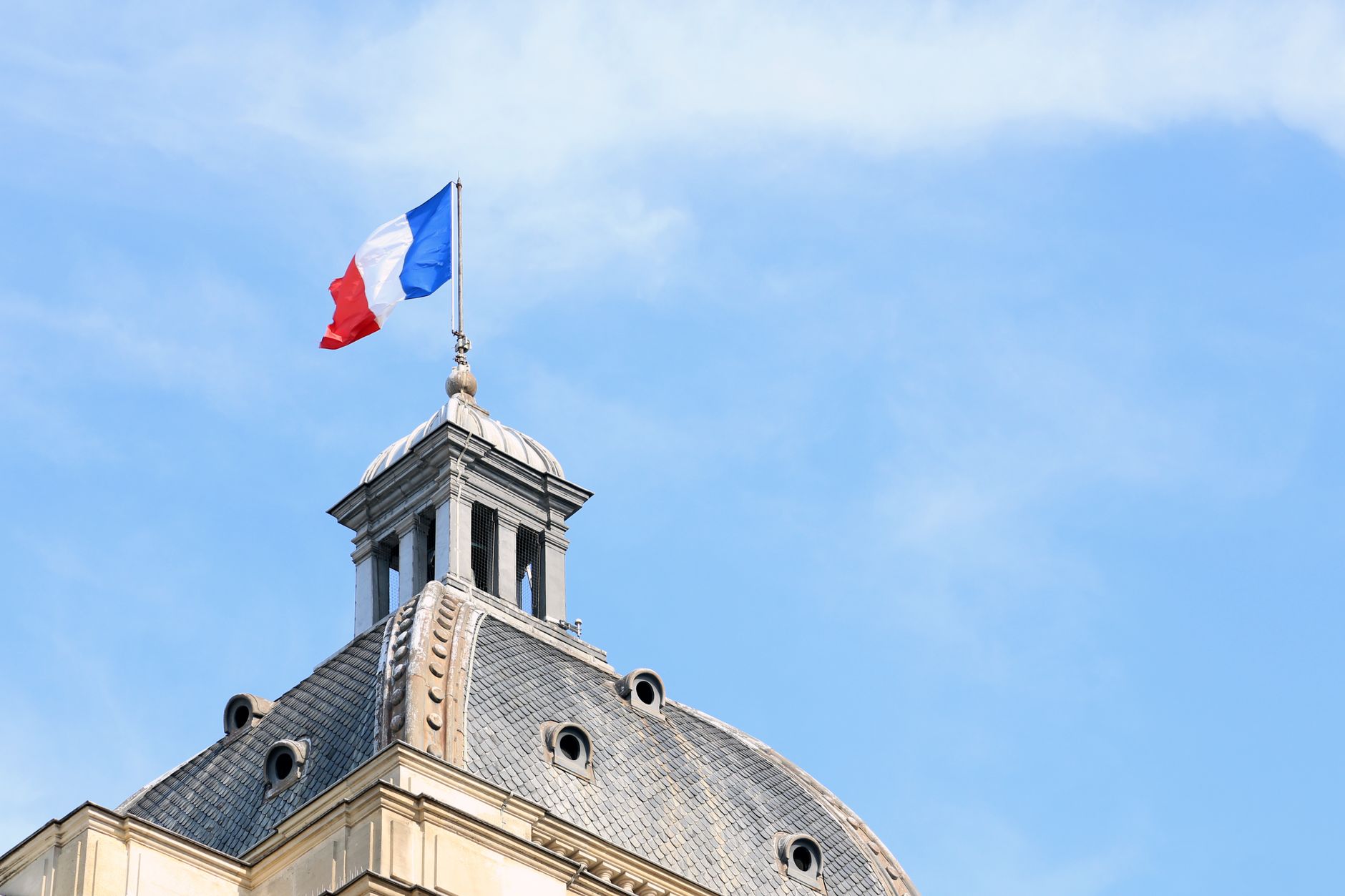 The French flag waves atop the dome of historic architecture in Paris, France.